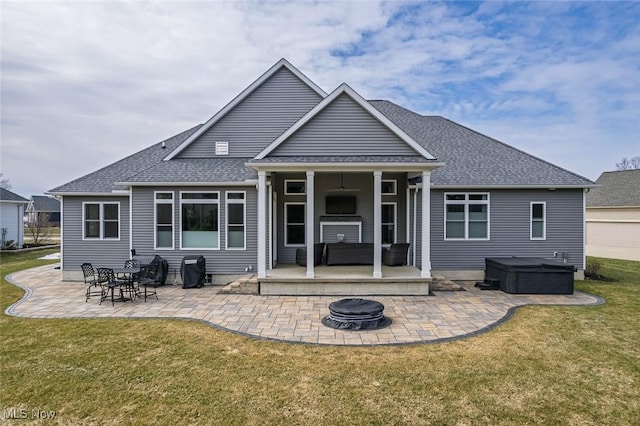 rear view of property featuring a patio, a lawn, a shingled roof, and a hot tub