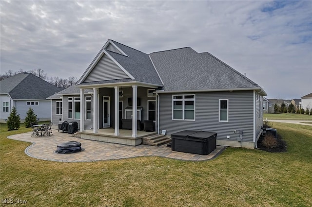 rear view of property featuring a patio, roof with shingles, a yard, a hot tub, and a fire pit