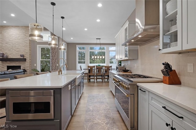 kitchen featuring a stone fireplace, light countertops, decorative backsplash, appliances with stainless steel finishes, and wall chimney exhaust hood