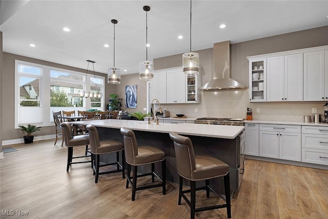 kitchen with a sink, an island with sink, wall chimney exhaust hood, and light countertops