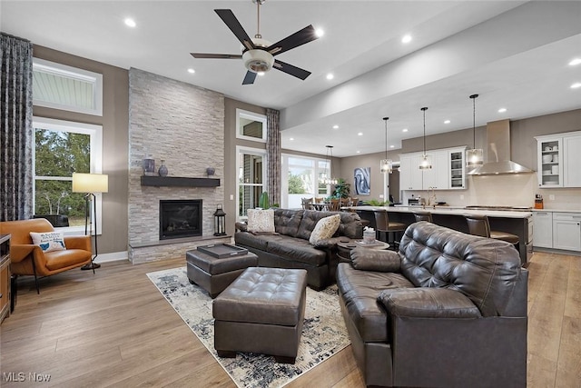 living room with a stone fireplace, recessed lighting, light wood finished floors, and ceiling fan