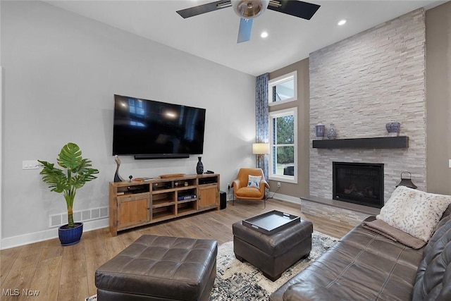 living room with visible vents, a stone fireplace, baseboards, and wood finished floors