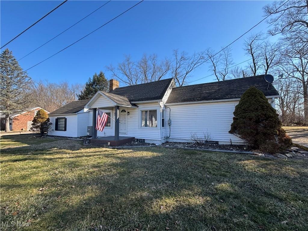 view of front facade featuring a chimney, a front lawn, and a shingled roof