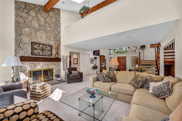 living room with carpet, beamed ceiling, stairway, a stone fireplace, and a towering ceiling