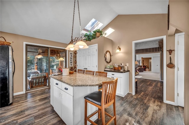 kitchen with a kitchen island, lofted ceiling with skylight, freestanding refrigerator, white cabinetry, and dark wood-style flooring