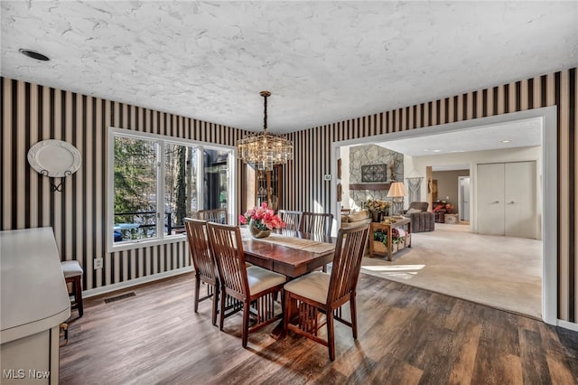 dining area featuring visible vents, wallpapered walls, baseboards, wood finished floors, and a notable chandelier