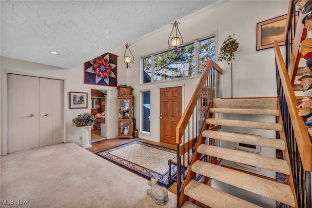 foyer entrance featuring stairway, carpet floors, a textured ceiling, and a towering ceiling