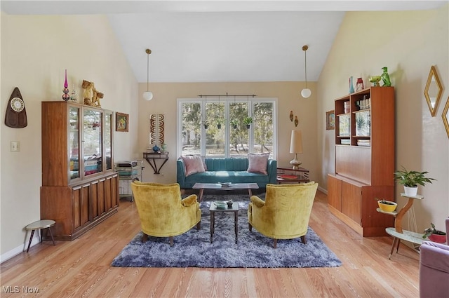 living area featuring baseboards, light wood-style floors, and high vaulted ceiling