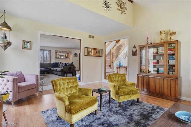 living area with stairway, light wood-style floors, visible vents, and baseboards