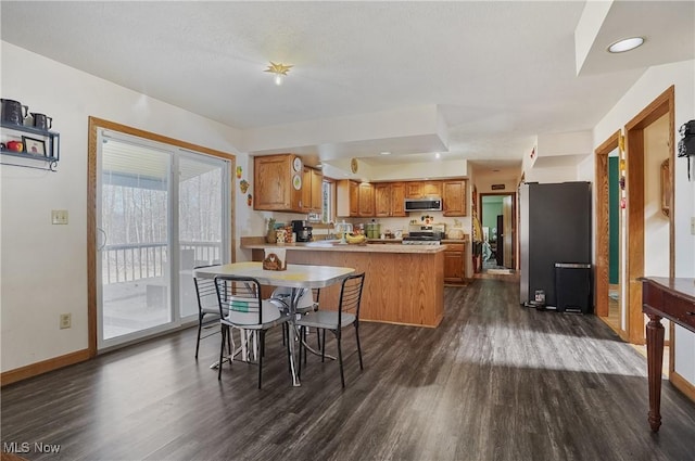 kitchen with dark wood-style floors, baseboards, a peninsula, stainless steel appliances, and brown cabinets