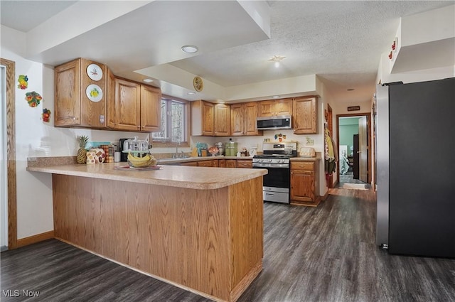 kitchen featuring dark wood finished floors, a peninsula, stainless steel appliances, light countertops, and a textured ceiling