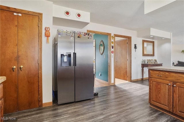 kitchen with dark wood finished floors, brown cabinetry, stainless steel fridge with ice dispenser, baseboards, and light countertops