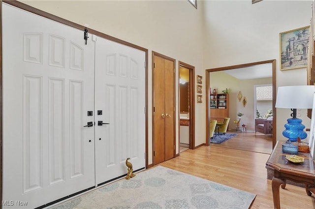 foyer featuring light wood-style floors, baseboards, and a towering ceiling