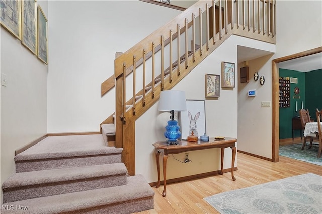 stairway with baseboards, wood finished floors, and a towering ceiling