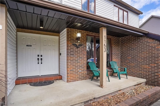 view of exterior entry featuring brick siding and a porch