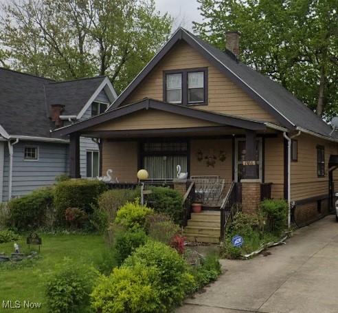 bungalow-style house featuring covered porch, driveway, and a chimney