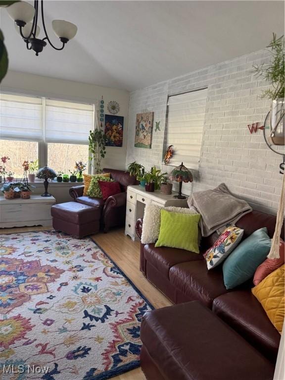 living room featuring a notable chandelier, brick wall, and wood finished floors