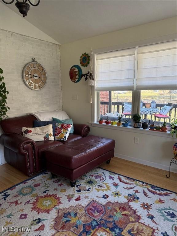 living area with vaulted ceiling, wood finished floors, baseboards, and brick wall