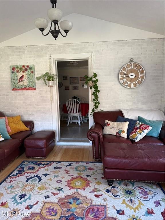 living room featuring lofted ceiling, wood finished floors, brick wall, and a chandelier