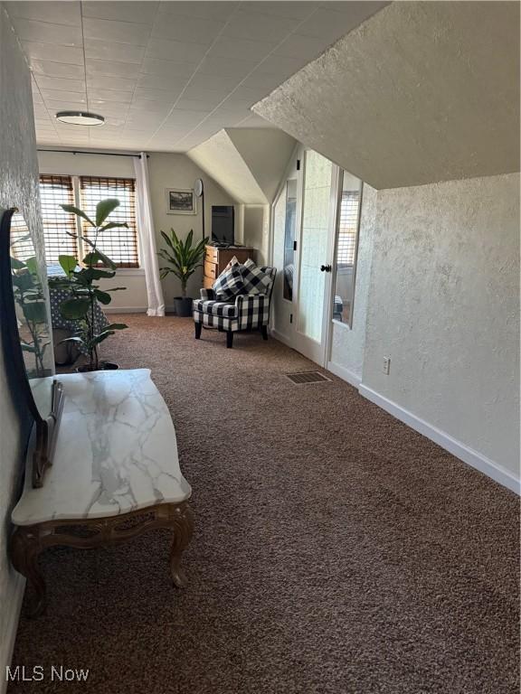 interior space with visible vents, a textured wall, carpet flooring, baseboards, and vaulted ceiling