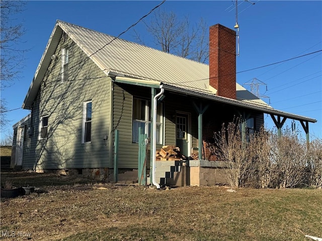 view of side of property featuring covered porch, a chimney, a lawn, and metal roof