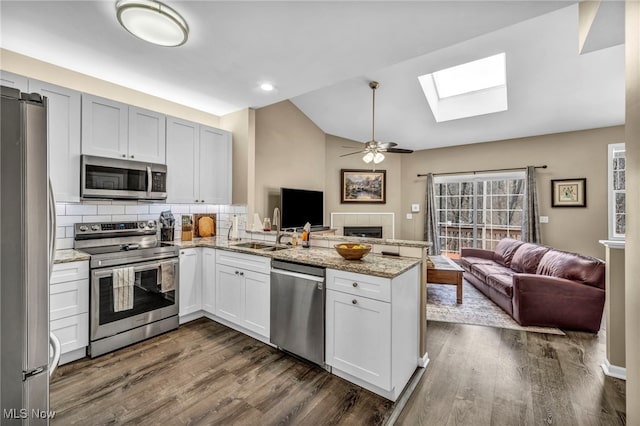 kitchen featuring a peninsula, vaulted ceiling with skylight, a sink, appliances with stainless steel finishes, and open floor plan