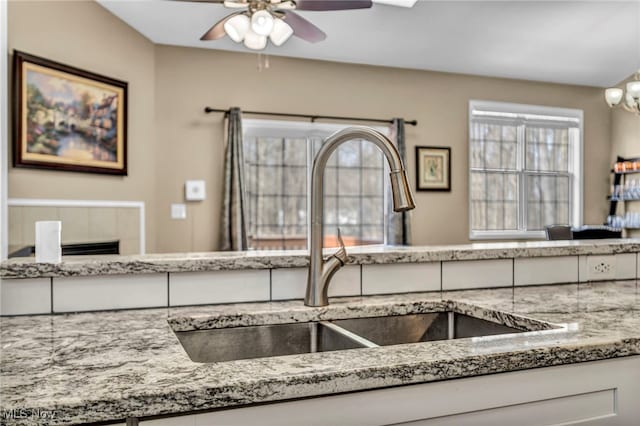 kitchen with a ceiling fan, stone counters, and a sink