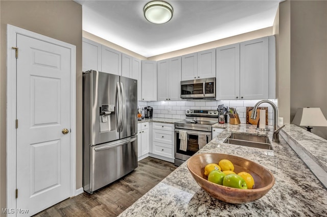 kitchen with light stone countertops, dark wood finished floors, a sink, appliances with stainless steel finishes, and tasteful backsplash