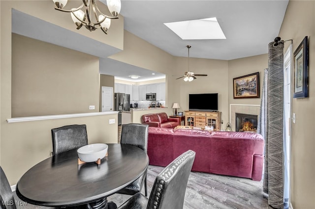 dining area with a skylight, light wood-style floors, ceiling fan, and a tiled fireplace