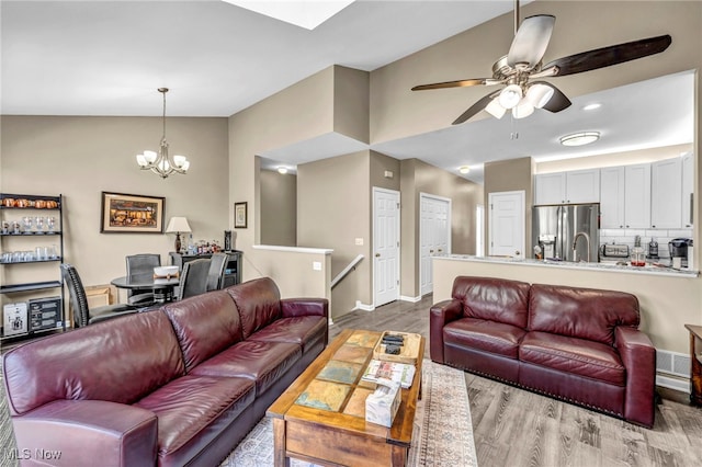 living room with visible vents, baseboards, vaulted ceiling, ceiling fan with notable chandelier, and wood finished floors