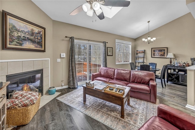 living room with lofted ceiling, a tiled fireplace, ceiling fan with notable chandelier, wood finished floors, and baseboards