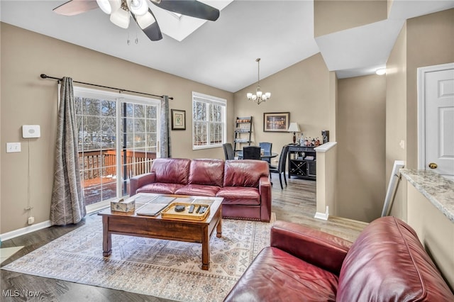 living room featuring baseboards, ceiling fan with notable chandelier, wood finished floors, and vaulted ceiling