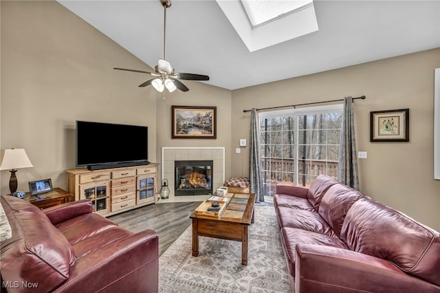 living room with a ceiling fan, wood finished floors, a fireplace, and lofted ceiling with skylight