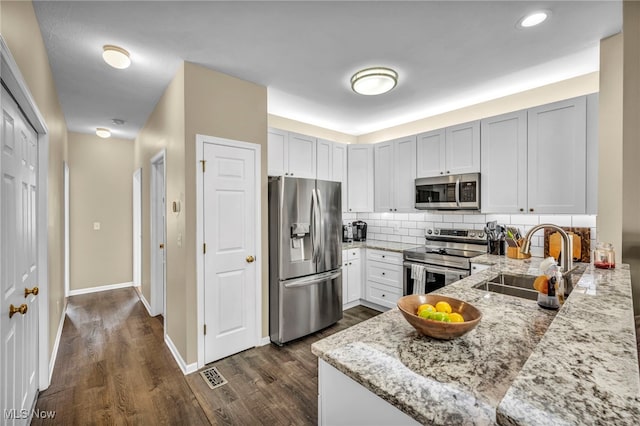 kitchen with light stone counters, decorative backsplash, dark wood-style floors, stainless steel appliances, and a sink