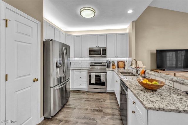 kitchen with tasteful backsplash, appliances with stainless steel finishes, a peninsula, wood finished floors, and a sink