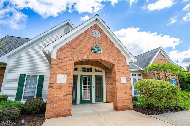 entrance to property featuring french doors, brick siding, and a shingled roof