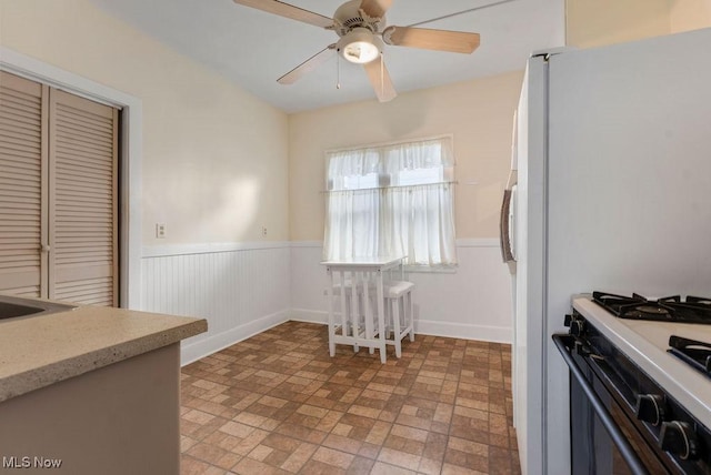 kitchen featuring gas range oven, ceiling fan, wainscoting, and freestanding refrigerator