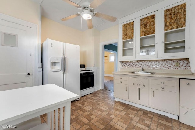 kitchen featuring glass insert cabinets, light countertops, range with gas stovetop, white refrigerator with ice dispenser, and a sink