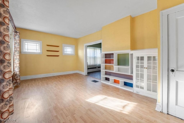 unfurnished living room featuring visible vents, a baseboard heating unit, baseboards, and wood finished floors