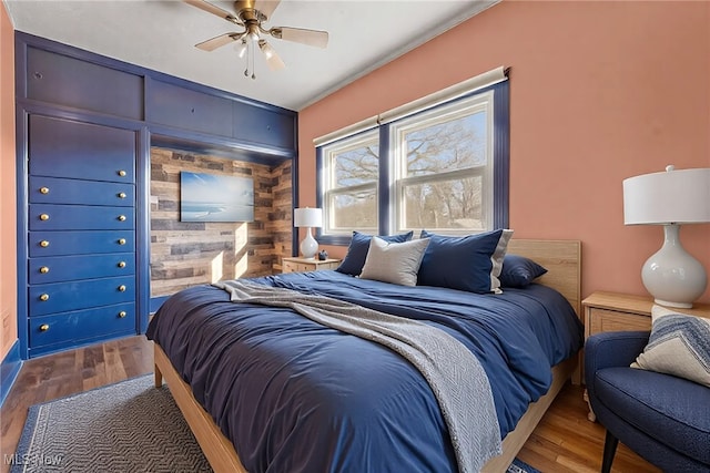 bedroom with a ceiling fan, wooden walls, wood finished floors, and an accent wall