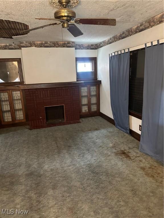 unfurnished living room with a ceiling fan, a textured ceiling, carpet floors, baseboards, and a brick fireplace