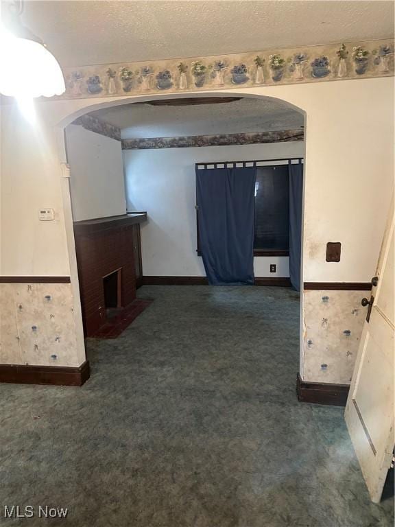 interior space with arched walkways, a wainscoted wall, a textured ceiling, and dark colored carpet