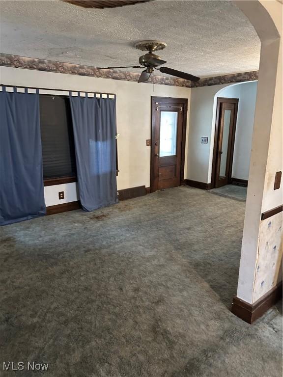 interior space with ceiling fan, baseboards, carpet floors, arched walkways, and a textured ceiling