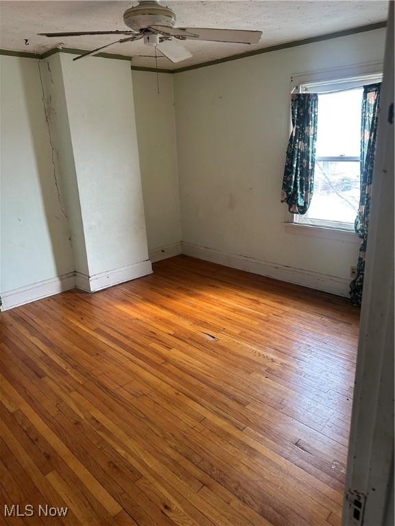 spare room featuring baseboards, light wood-type flooring, and ceiling fan