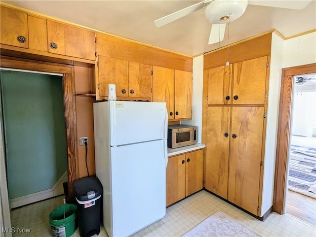 kitchen featuring stainless steel microwave, light floors, brown cabinets, freestanding refrigerator, and a ceiling fan