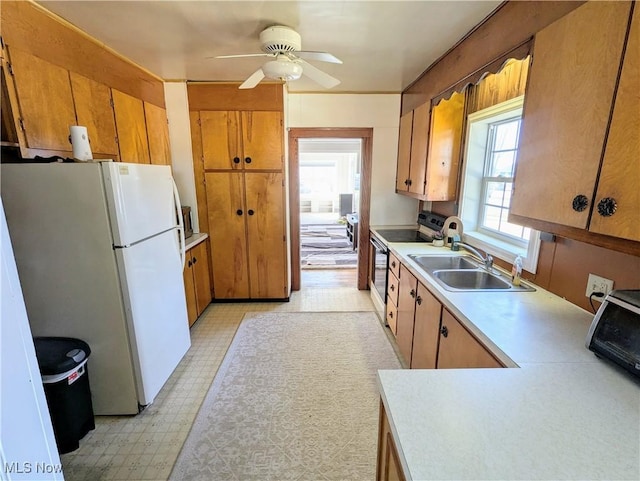 kitchen featuring light floors, light countertops, electric range oven, brown cabinets, and freestanding refrigerator