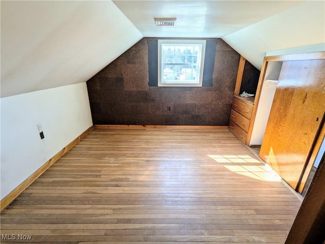 bonus room with light wood-type flooring, baseboards, lofted ceiling, and visible vents