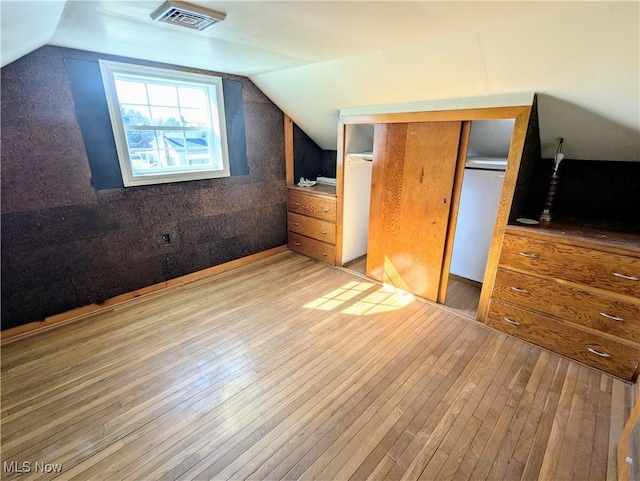 unfurnished bedroom with vaulted ceiling, visible vents, a closet, and wood-type flooring