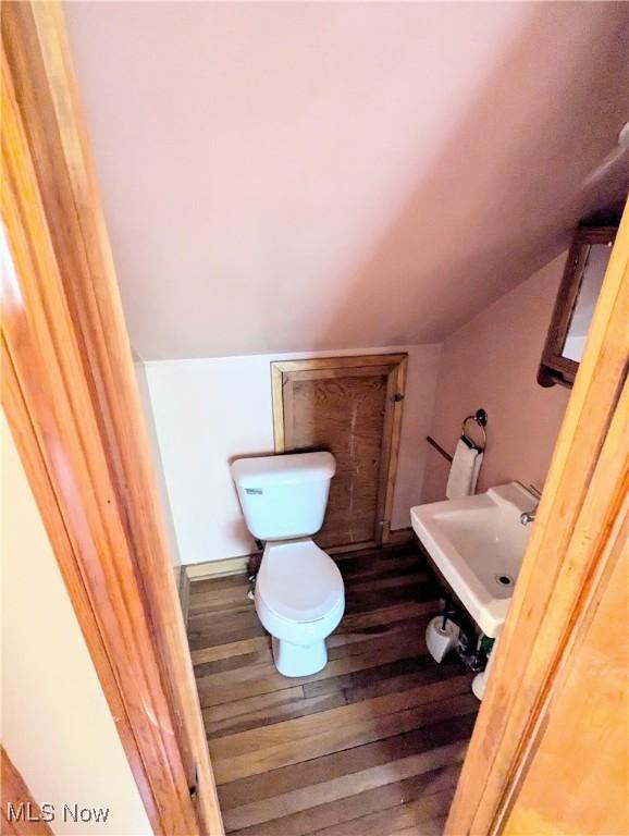 half bathroom with a sink, wood finished floors, and vaulted ceiling