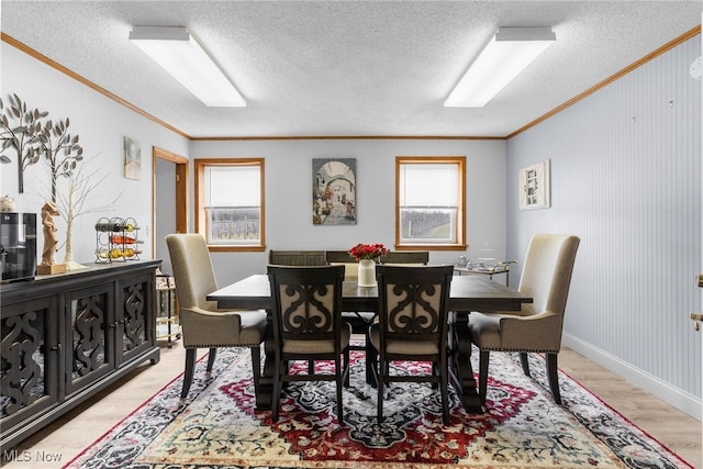 dining area with a textured ceiling, a healthy amount of sunlight, ornamental molding, and light wood finished floors